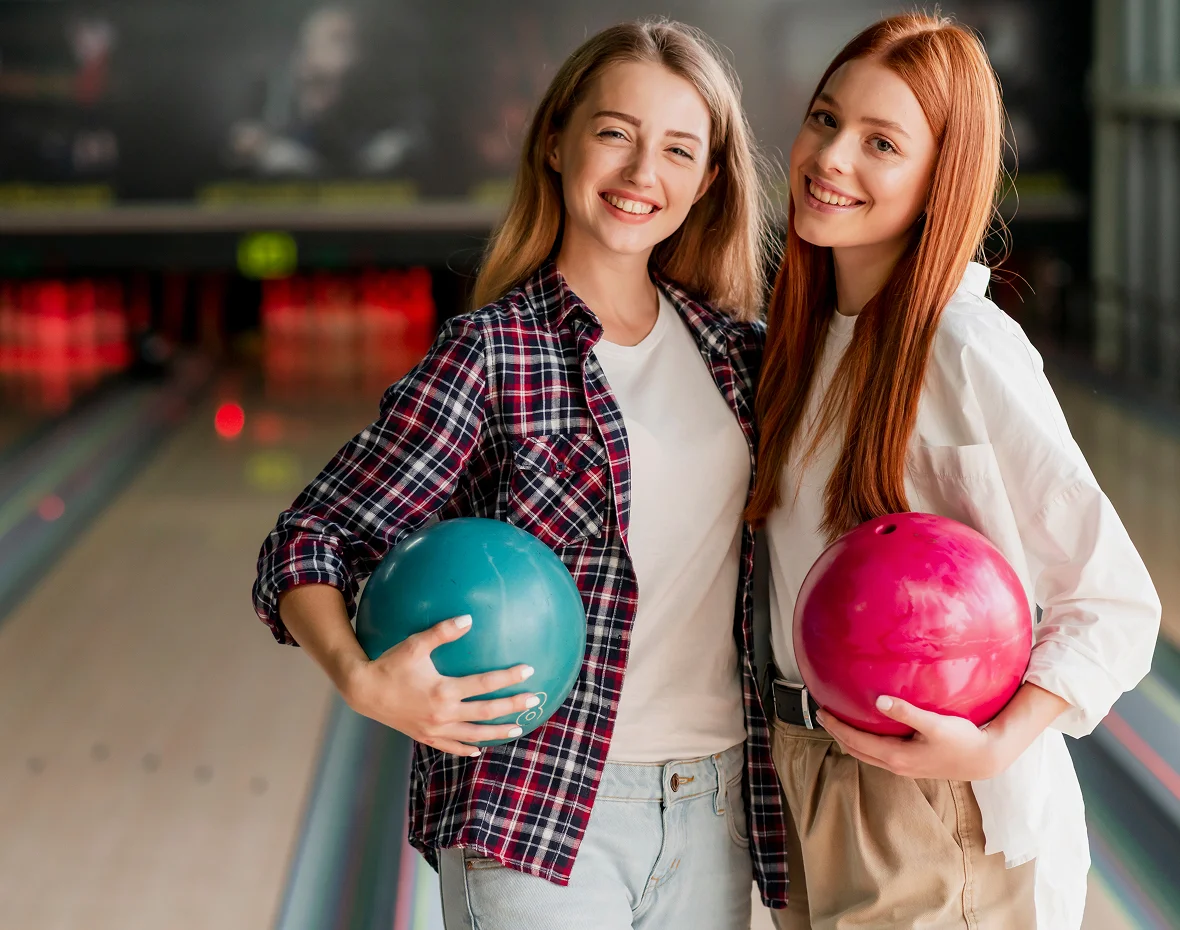 Dos amigas con bolas de bolos en una bolera
